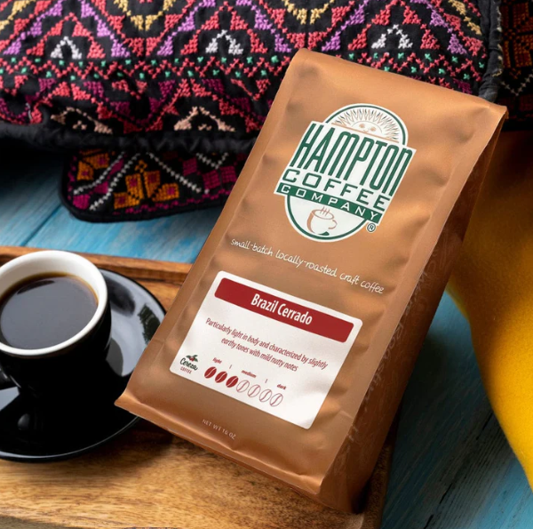 Bag of Hampton Coffee Company Brazil Cerrado direct trade coffee on a wooden tray beside a cup of black coffee